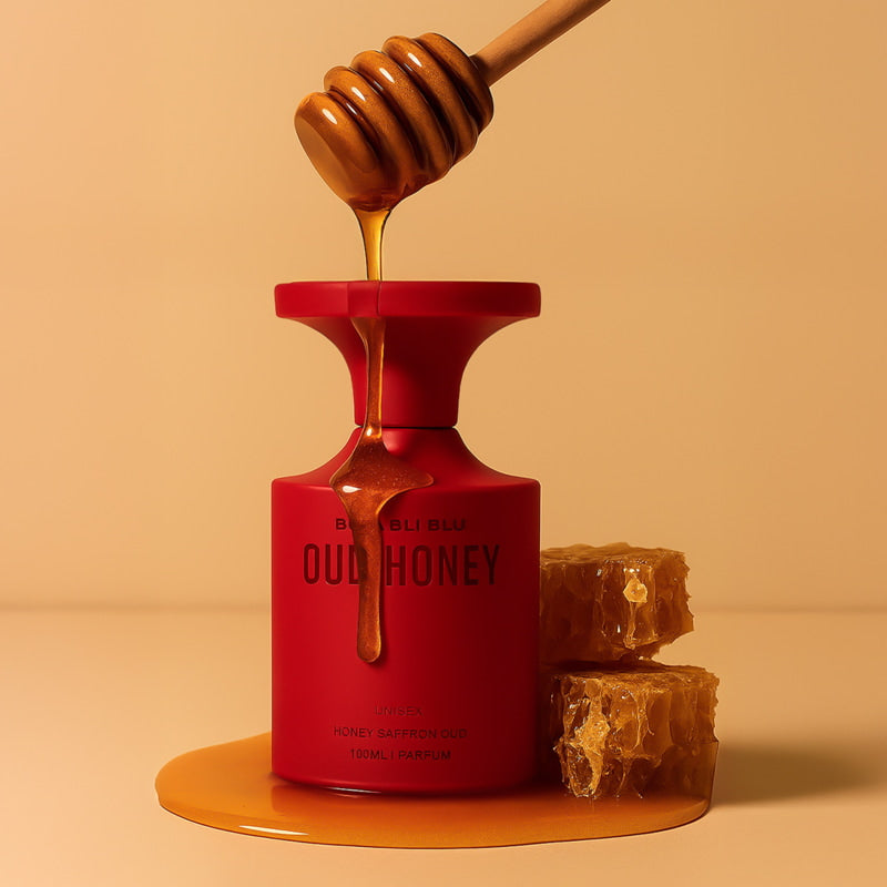 Red bottle labeled 'honey oud perfume' with being dripped from a wooden dipper onto a beige background.